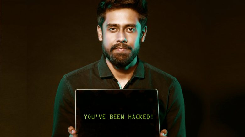 Ein Mann hält einen Laptop. Auf dem Bildschirm steht: "You've been hacked"