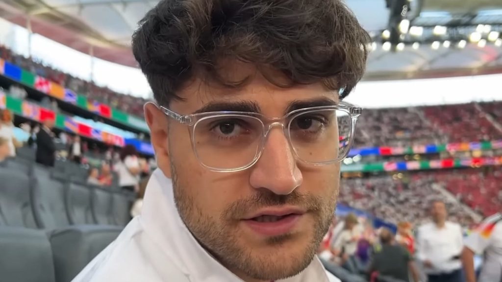 Titel EliasN97 mit Brille und Deutschlandjacke in vollem Stadion