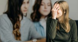 Junge Frau beobachtet von zwei anderen Frauen, Symbolbild